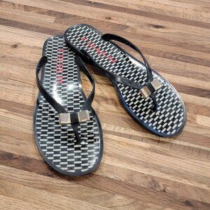 Coach Landon jelly flip flops in black with a gold bow and white pattern.